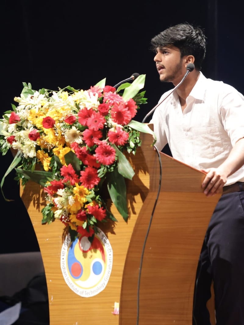Adari Karthikeya speaking at a flower-decked podium at IIT Guwahati